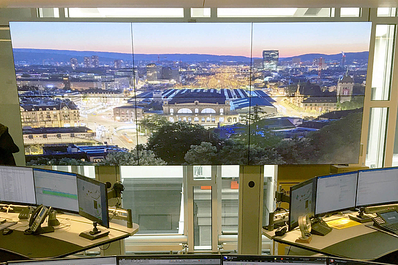 Zwei Arbeitsplätz vor einer großen Video Wall mit Bild vom Zürcher Hauptbahnhof