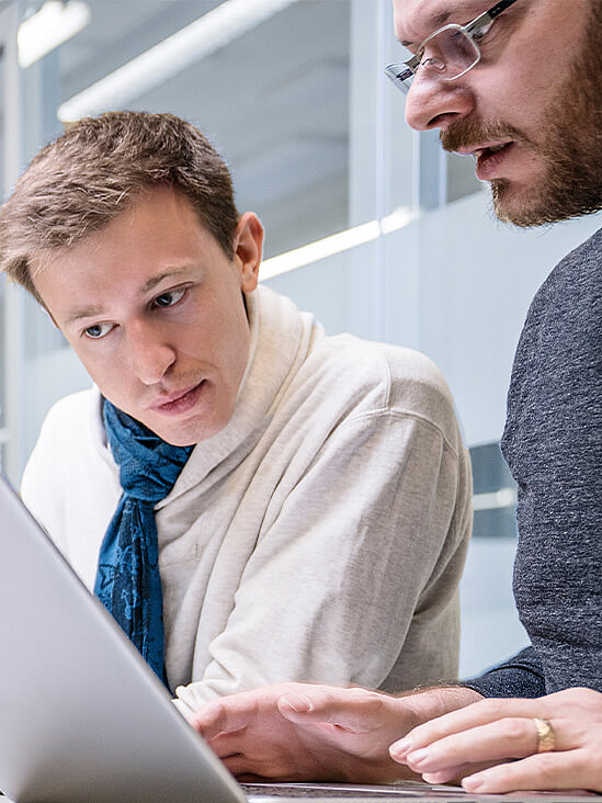 Two men at one laptop in office environment 